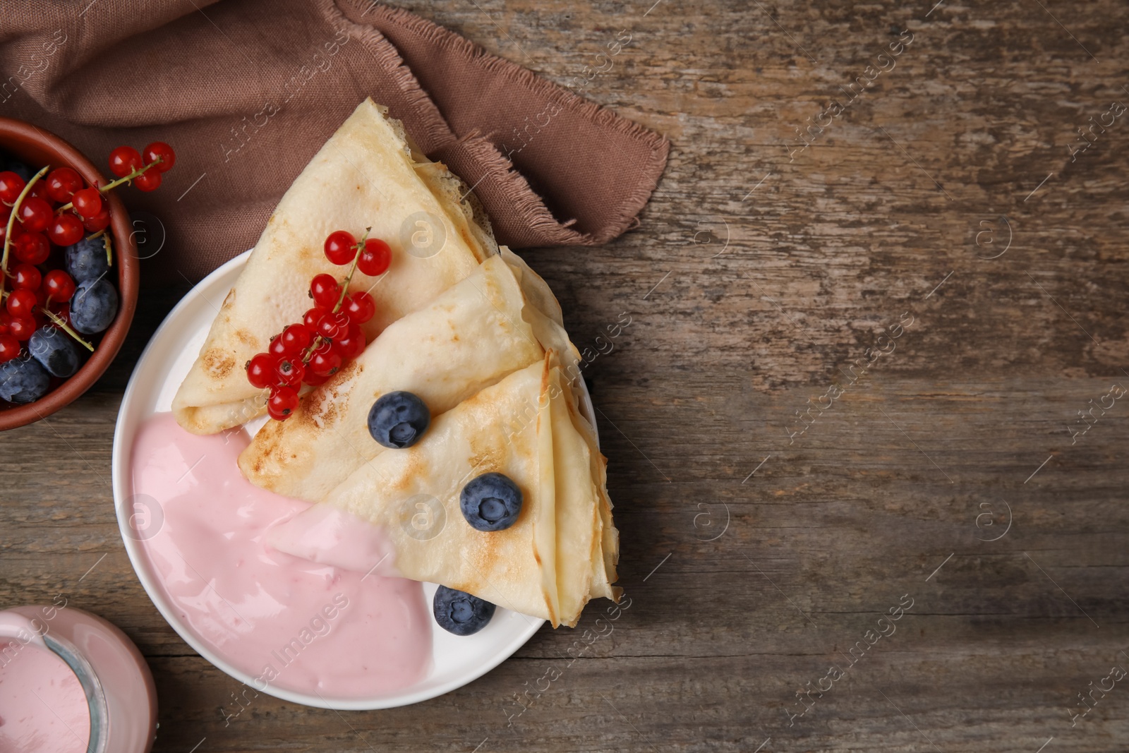 Photo of Delicious crepes with natural yogurt, blueberries and red currants on wooden table, flat lay. Space for text