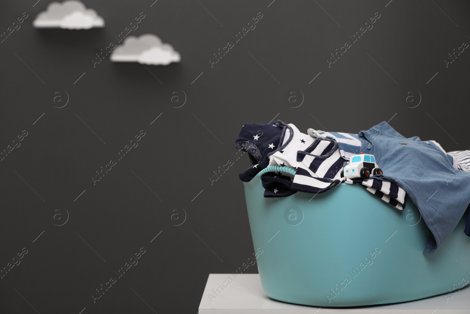 Photo of Laundry basket with baby clothes and toy car on white table against grey background, space for text