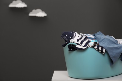 Laundry basket with baby clothes and toy car on white table against grey background, space for text