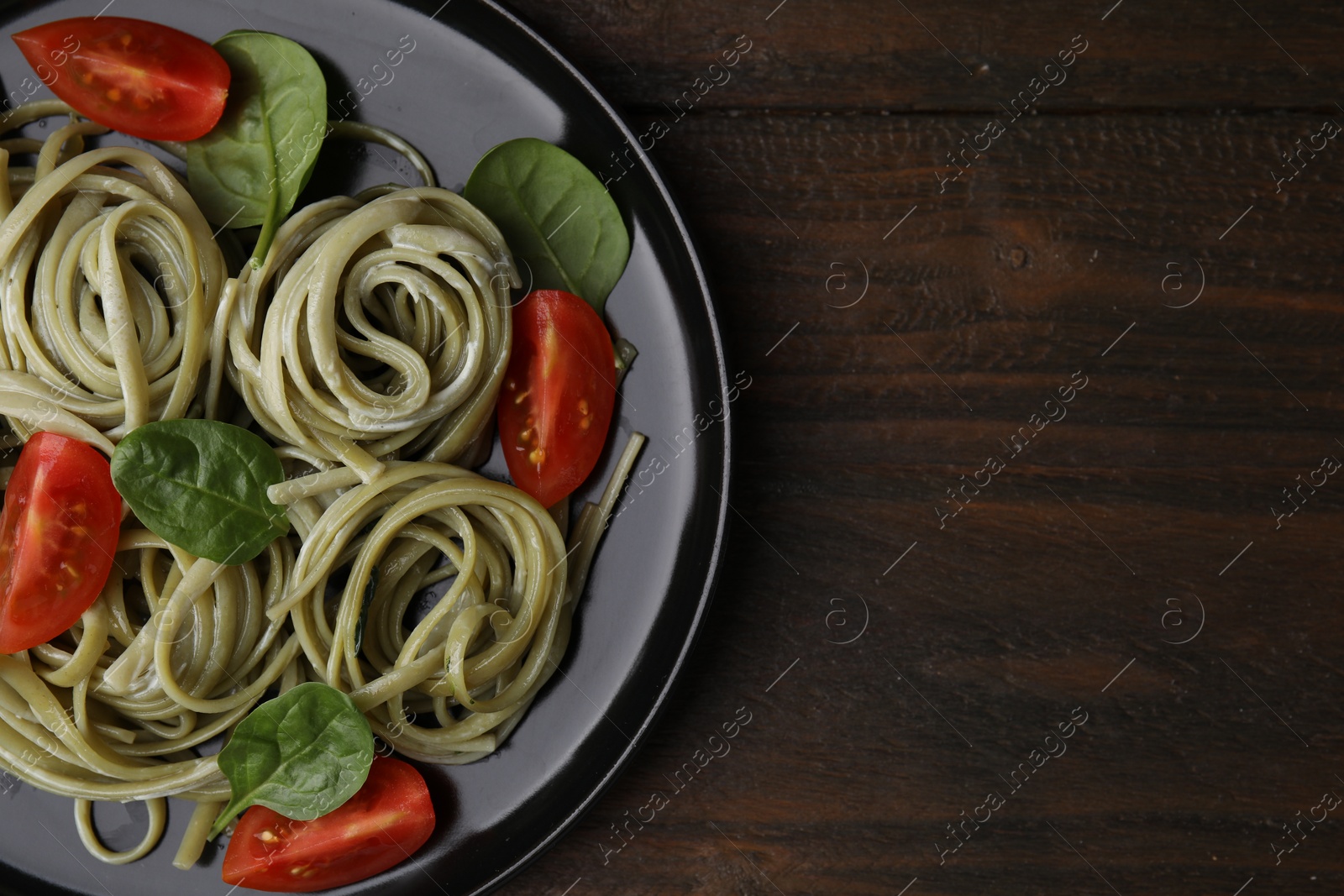 Photo of Tasty pasta with spinach, sauce and tomatoes on wooden table, top view. Space for text