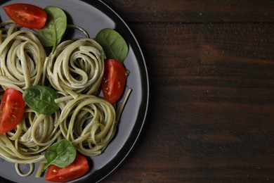 Photo of Tasty pasta with spinach, sauce and tomatoes on wooden table, top view. Space for text