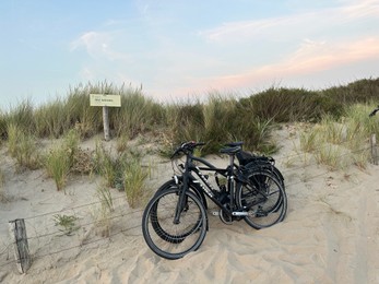 Two modern bicycles parked on sand outdoors
