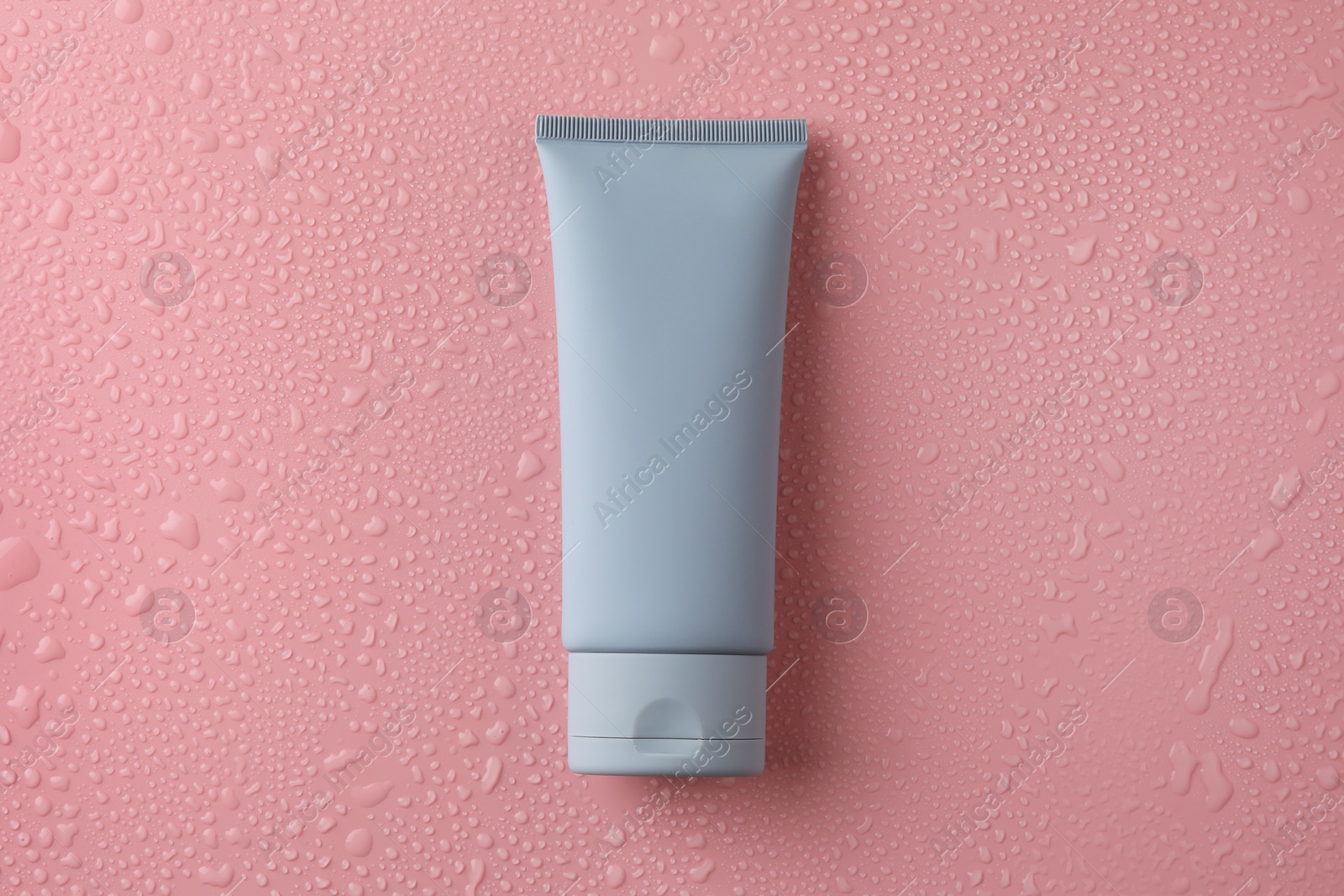 Photo of Moisturizing cream in tube on pink background with water drops, top view