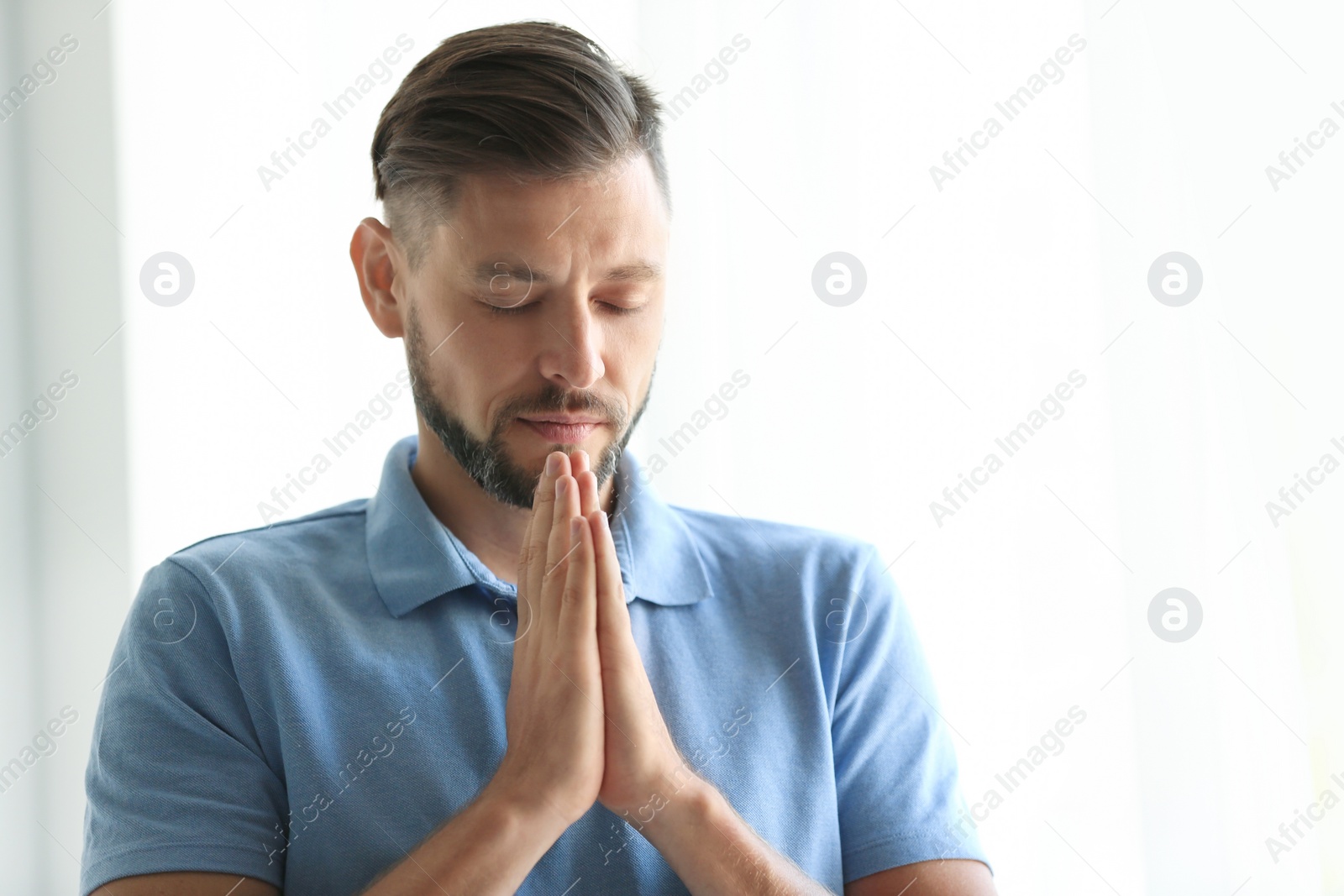 Photo of Man with hands clasped together for prayer on light background. Space for text