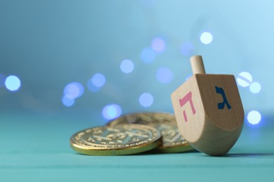 Photo of Hanukkah celebration. Wooden dreidel with jewish letters and coins against light blue background with blurred lights. Space for text