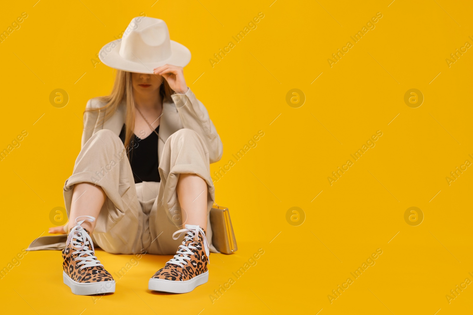 Photo of Stylish woman posing in classic old school sneakers with leopard print on orange background, selective focus. Space for text