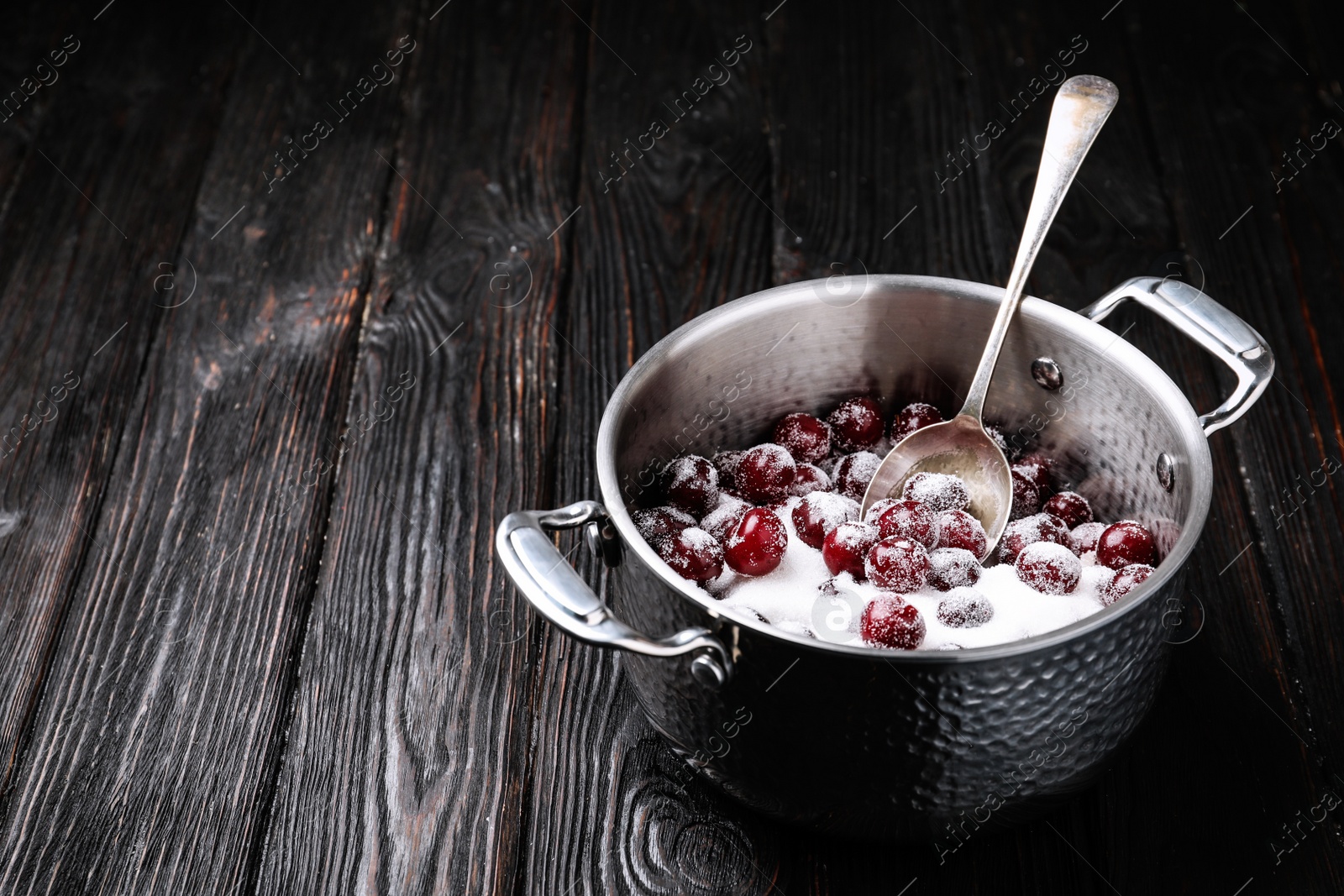 Photo of Pot with cherries and sugar on black wooden table, space for text. Making of delicious jam