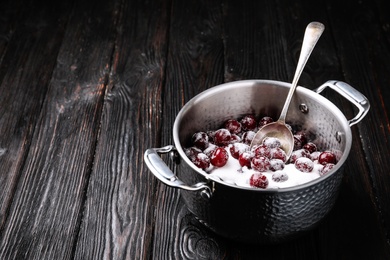 Photo of Pot with cherries and sugar on black wooden table, space for text. Making of delicious jam