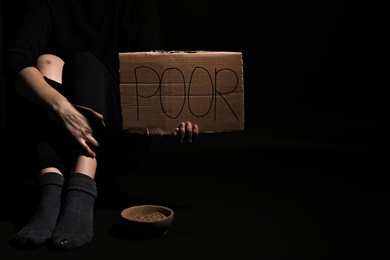 Woman holding cardboard sign with word "POOR" on dark background, closeup