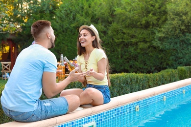 Happy couple with drinks at barbecue party near swimming pool outdoors