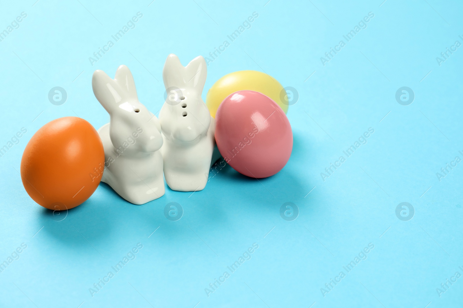 Photo of Ceramic Easter bunnies and dyed eggs on color background, space for text