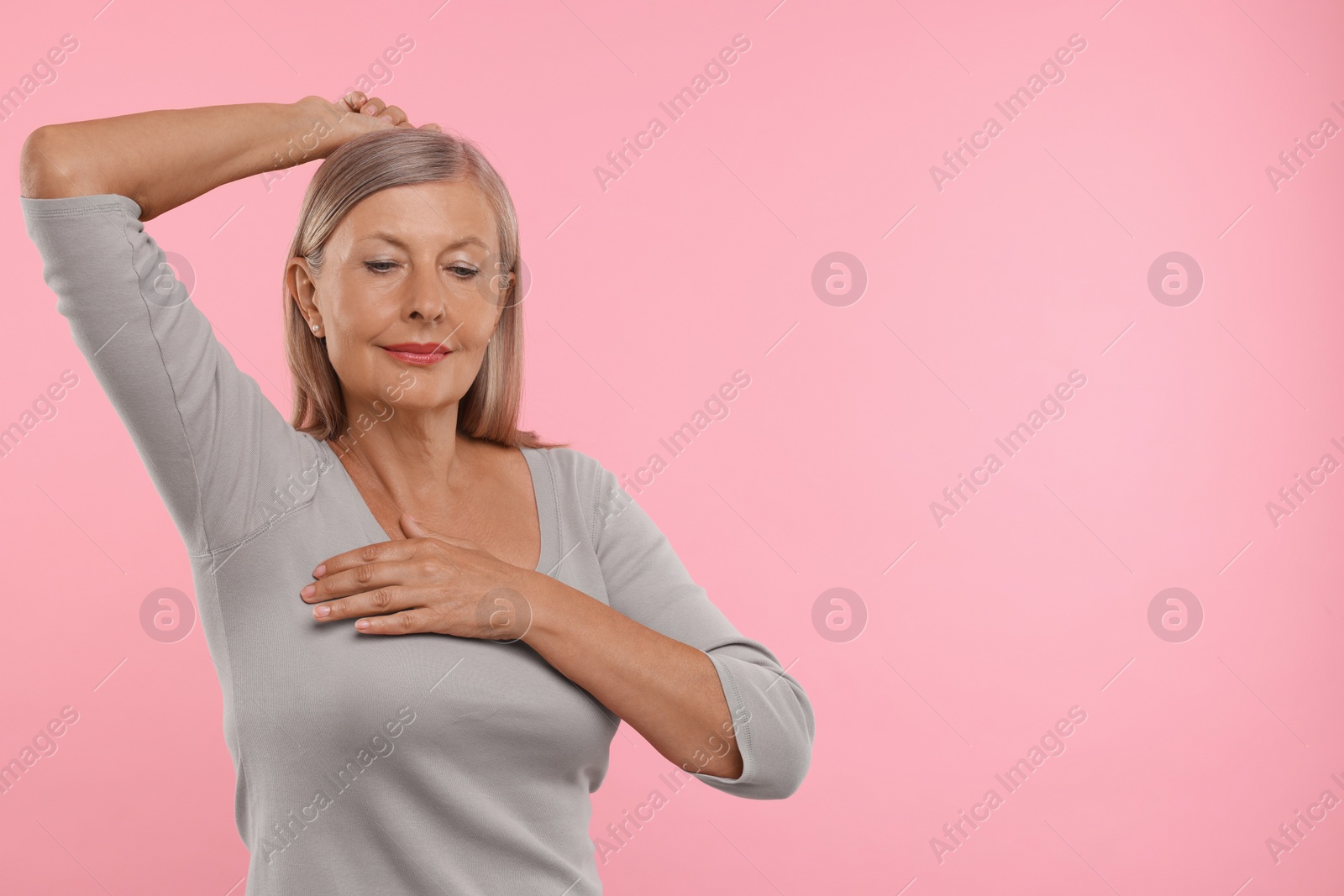 Photo of Beautiful senior woman doing breast self-examination on pink background, space for text