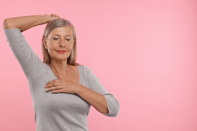 Beautiful senior woman doing breast self-examination on pink background, space for text