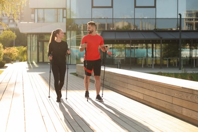 Photo of Happy couple practicing Nordic walking with poles outdoors on sunny day