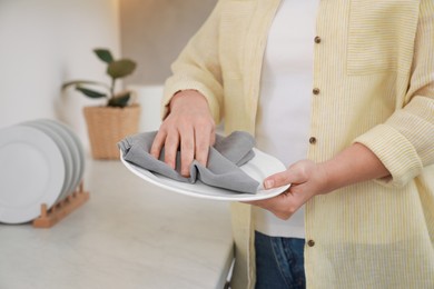 Woman wiping plate with towel at white marble table in kitchen, closeup