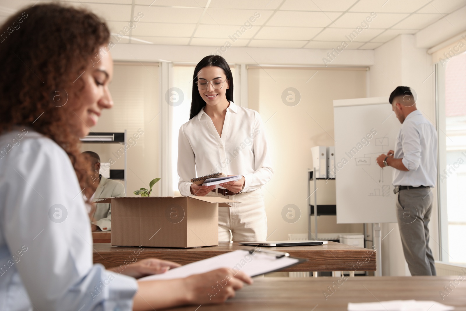 Photo of New coworker unpacking box with personal items at workplace in office