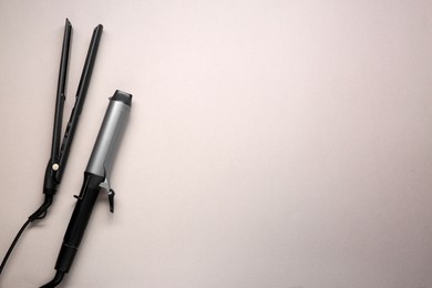 Photo of Curling iron and hair straightener on grey background, flat lay. Space for text