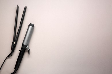 Curling iron and hair straightener on grey background, flat lay. Space for text