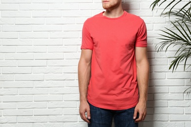 Young man wearing blank t-shirt near white brick wall, closeup. Mockup for design