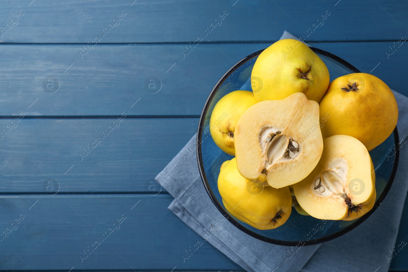 Photo of Tasty ripe quinces in bowl on blue wooden table, top view. Space for text