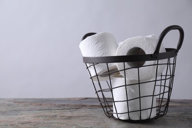 Toilet paper rolls in basket on textured table near light grey wall, space for text