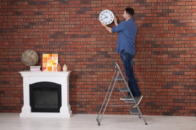 Photo of Man on stepladder hanging clock at home