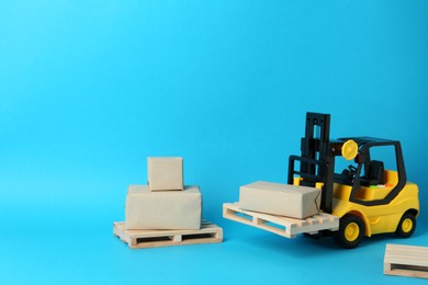 Toy forklift, wooden pallets and boxes on light blue background, space for text