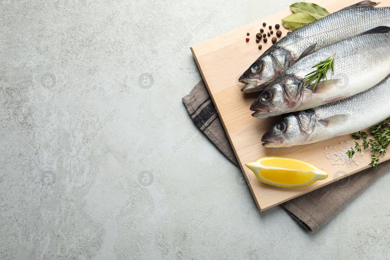 Photo of Tasty sea bass fish and spices on grey textured table, top view. Space for text