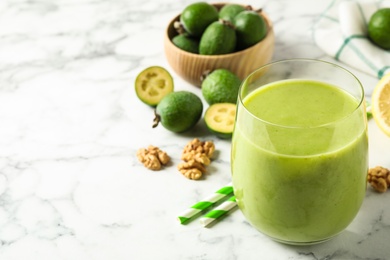 Photo of Fresh feijoa smoothie in glass on white marble table, closeup. Space for text