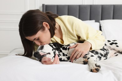 Photo of Beautiful woman kissing her adorable Dalmatian dog on bed at home. Lovely pet