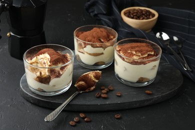 Delicious tiramisu in glasses, spoon and coffee beans on black table