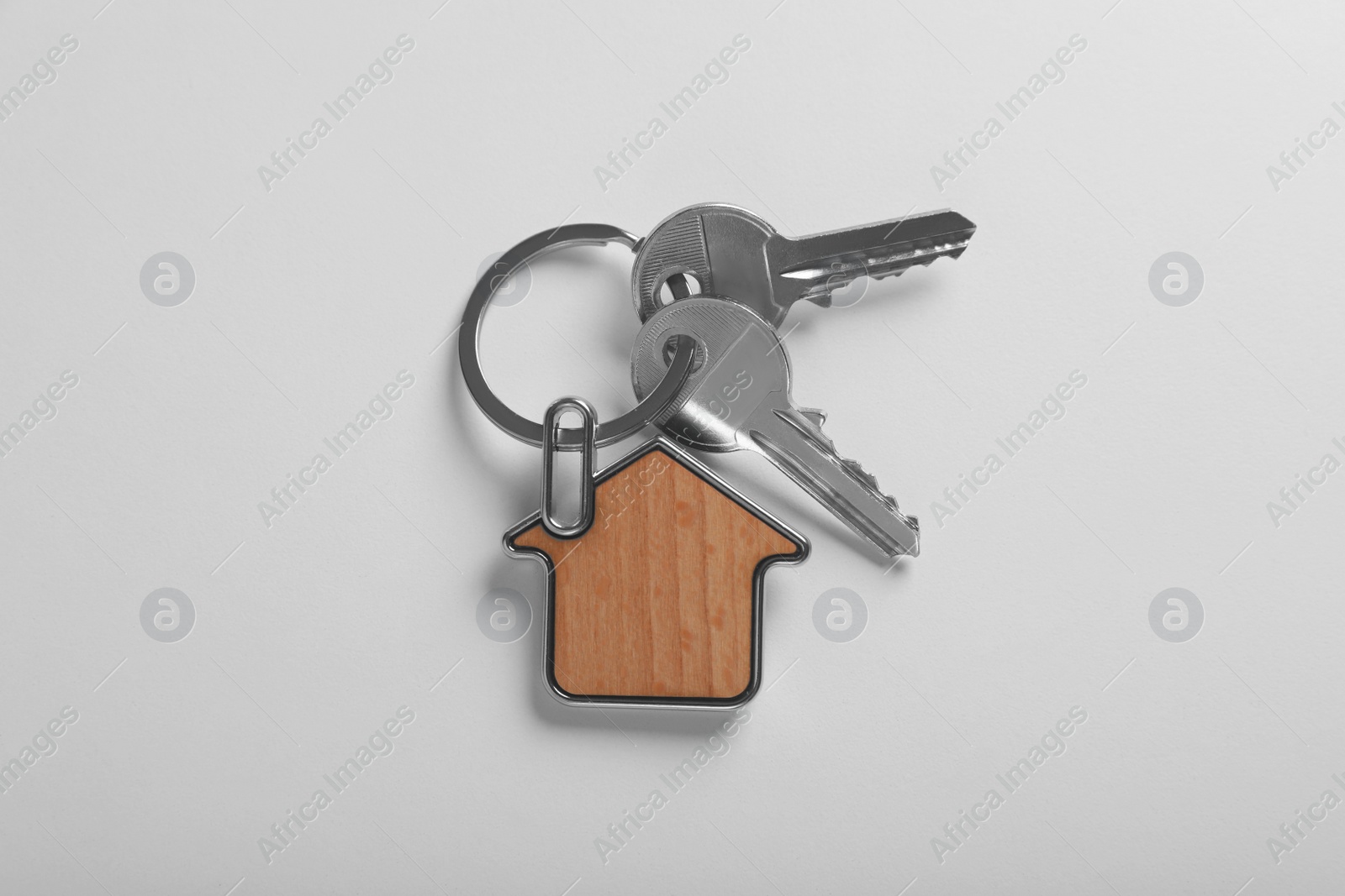 Photo of Keys with trinket in shape of house on white background, top view. Real estate agent services