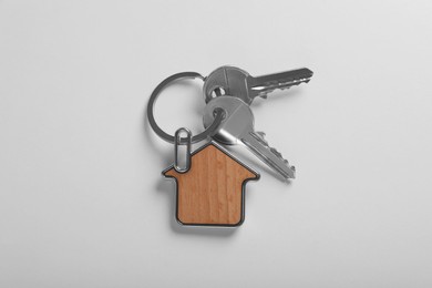 Keys with trinket in shape of house on white background, top view. Real estate agent services