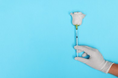 Photo of Doctor making injection to rose on light blue background, top view. Space for text