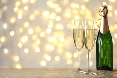 Photo of Glasses and bottle of champagne on table against blurred lights. Space for text