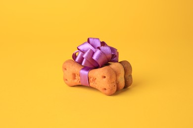 Photo of Bone shaped dog cookies with purple bow on yellow background