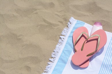 Photo of Striped towel with bottle of sunblock and flip flops on sandy beach, flat lay. Space for text