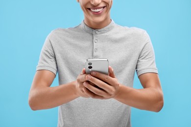 Young man sending message via smartphone on light blue background, closeup