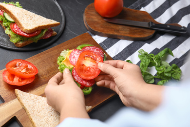 Photo of Woman adding tomato to sandwich at black table, closeup