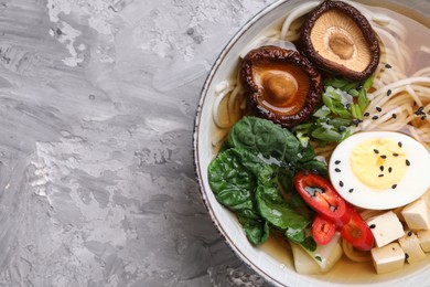 Delicious vegetarian ramen with egg, mushrooms, tofu and vegetables in bowl on grey table, top view and space for text. Noodle soup