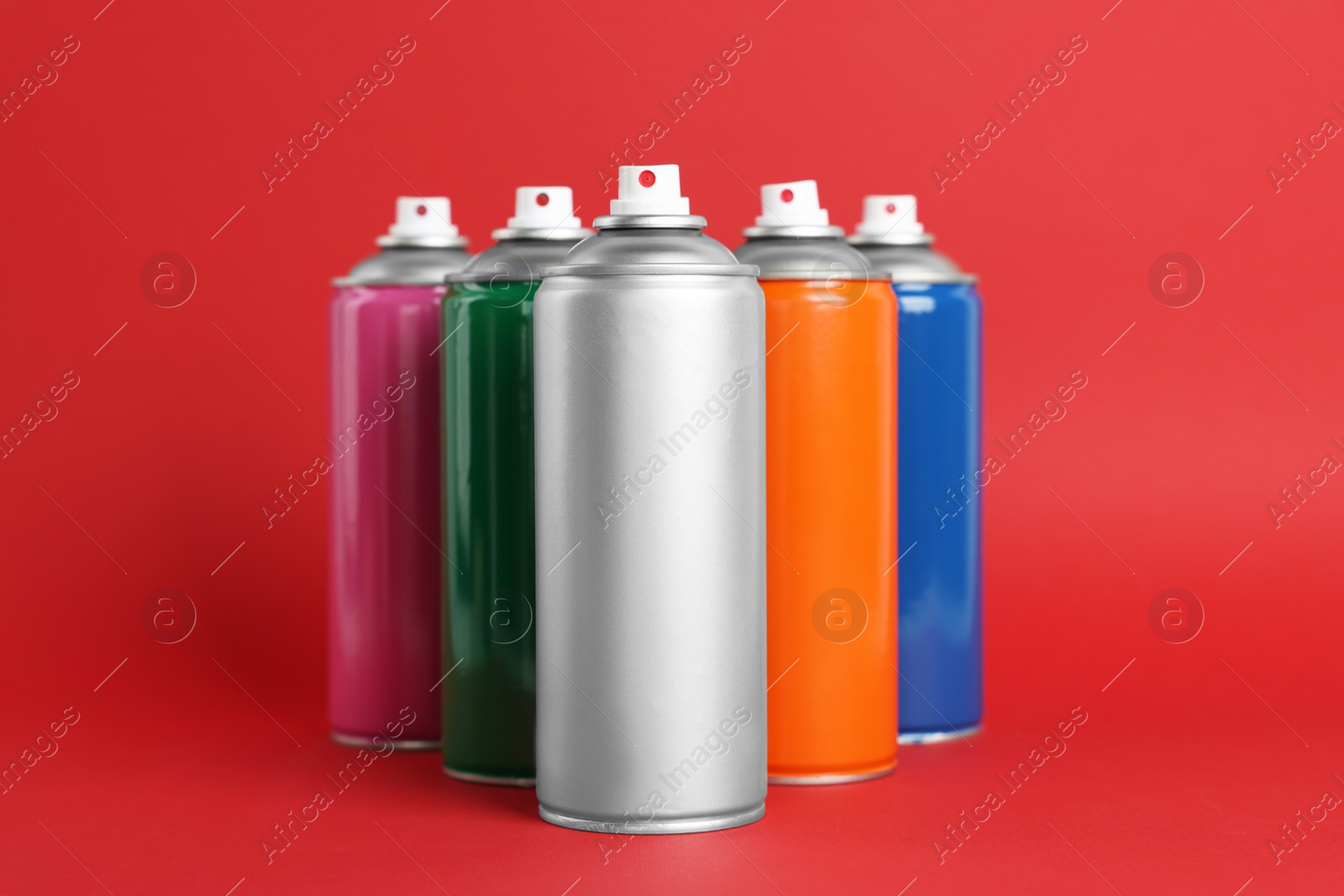 Photo of Colorful cans of spray paints on red background