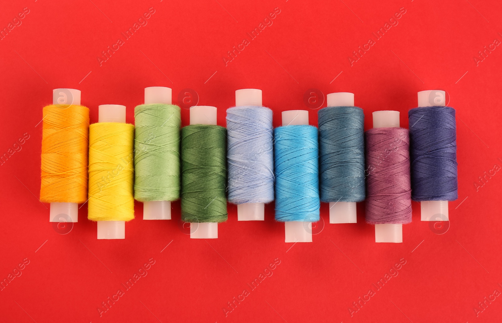 Photo of Different colorful sewing threads on red background, flat lay