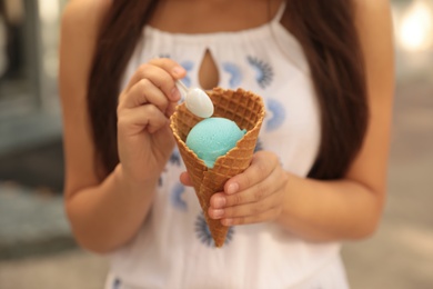 Photo of Young woman with delicious ice cream in waffle cone outdoors, closeup