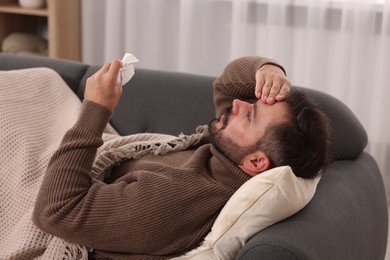 Photo of Sick man with tissue lying on sofa at home. Cold symptoms
