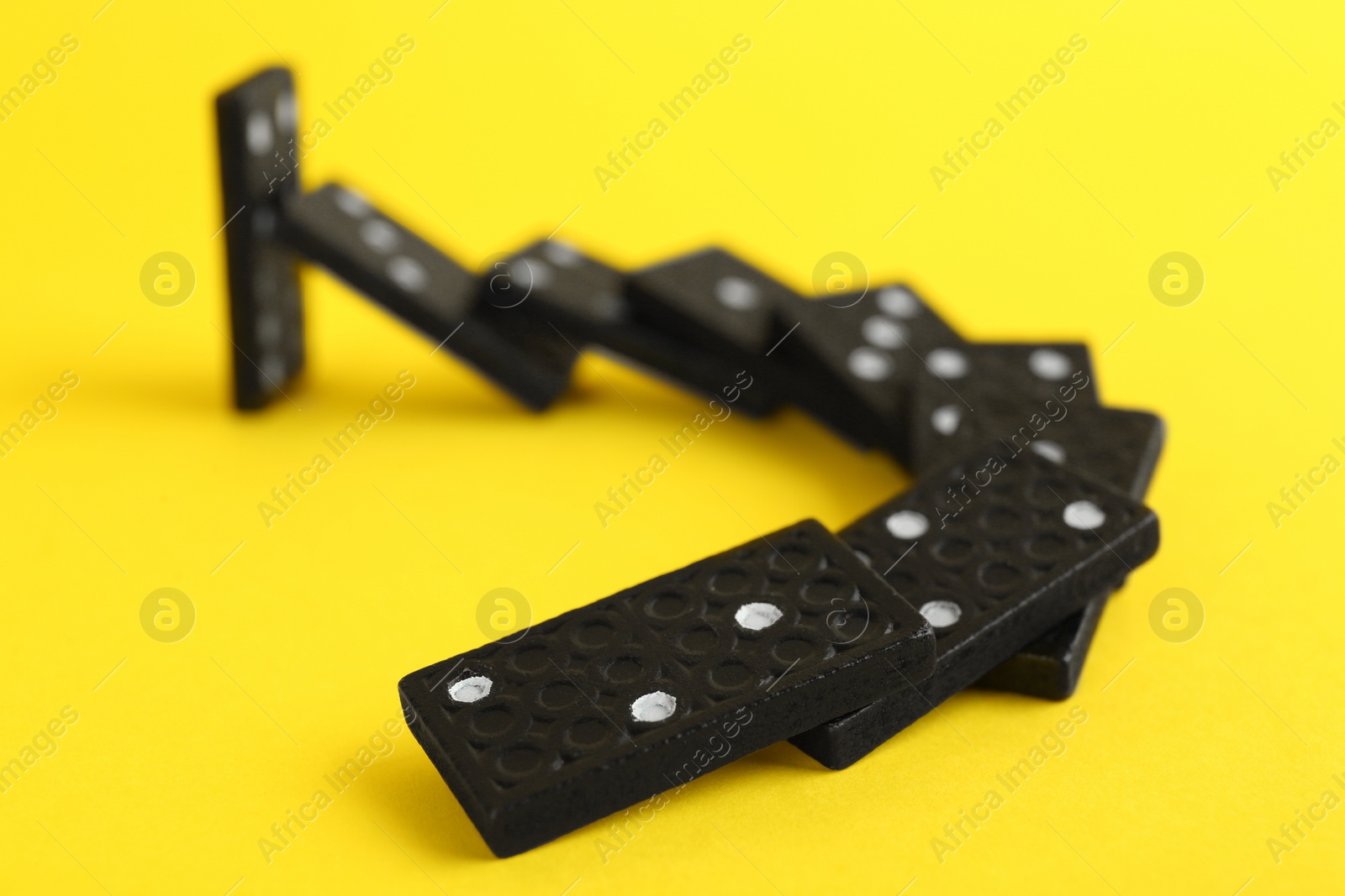 Photo of Black domino tiles falling on yellow background. Space for text