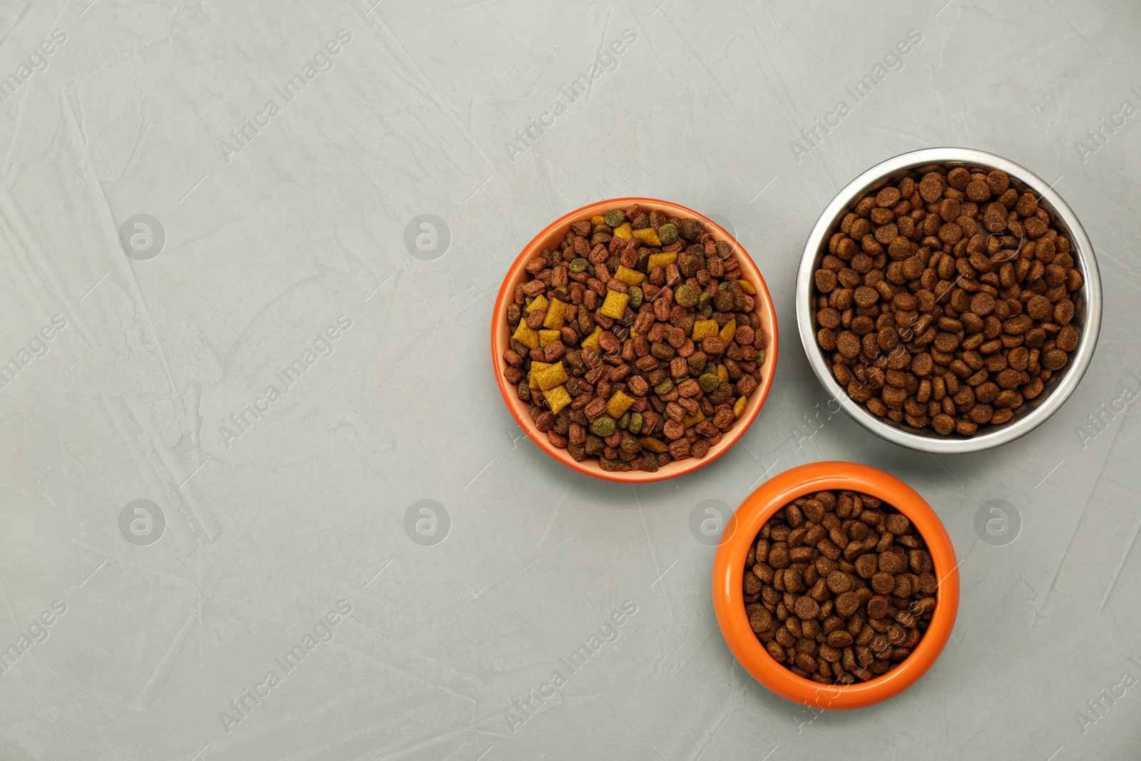 Photo of Dry food in pet bowls on grey background, flat lay. Space for text