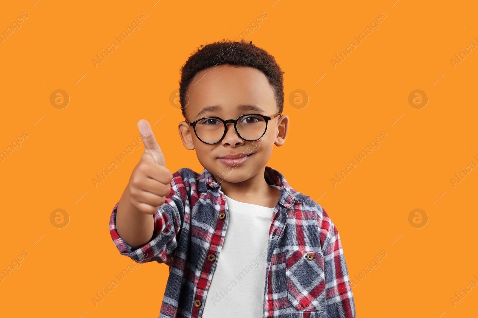 Photo of African-American boy with glasses showing thumb up on orange background