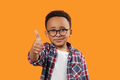 African-American boy with glasses showing thumb up on orange background