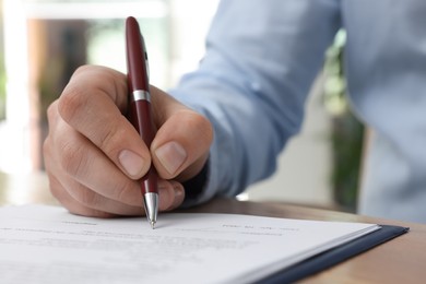 Man signing contract at table in office, closeup