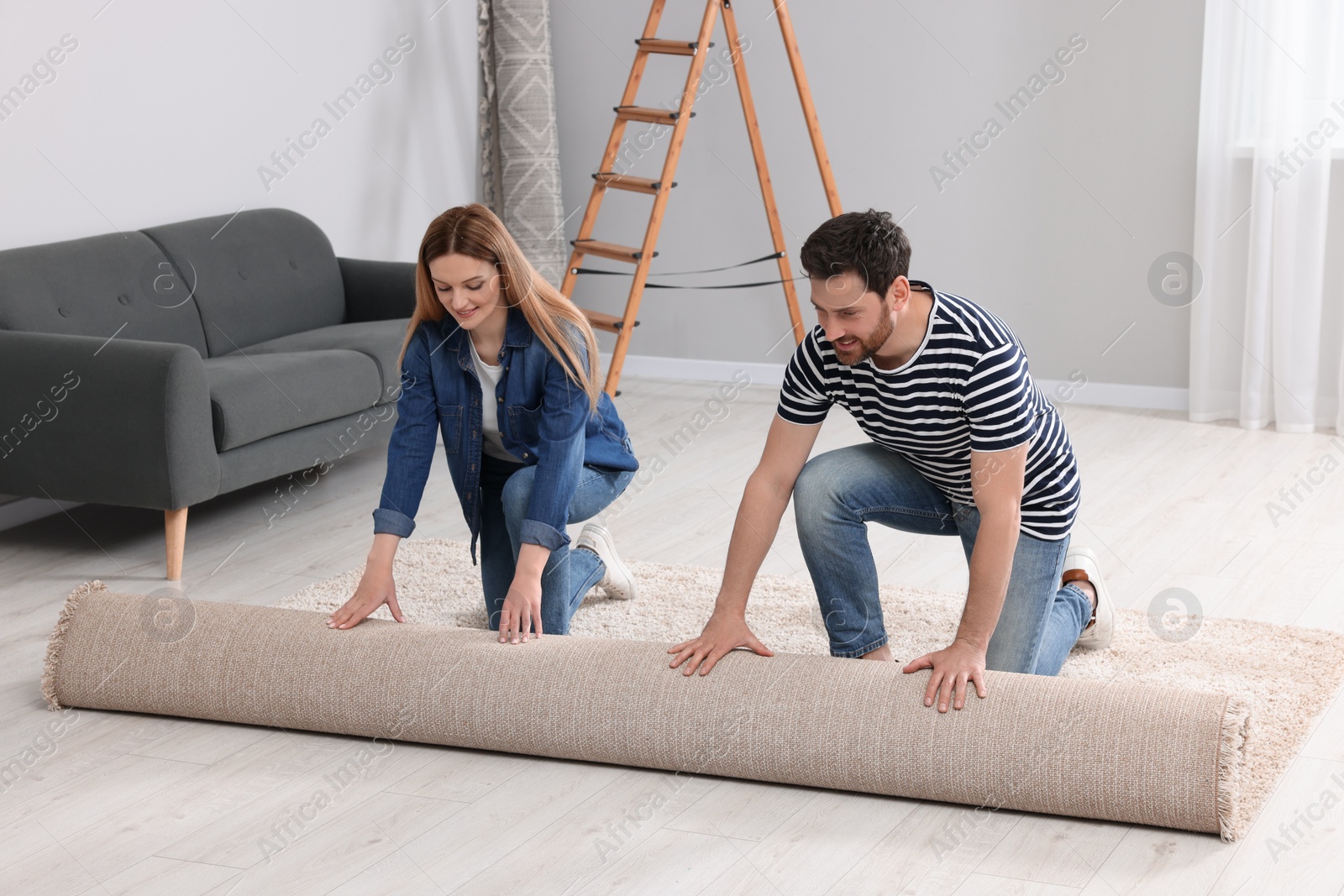 Photo of Smiling couple unrolling new carpet in room